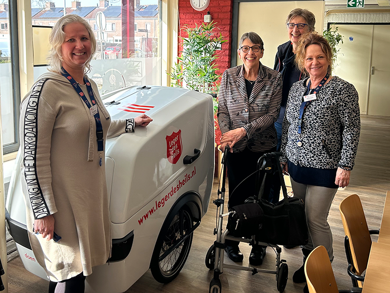 Jetta Klijnsma en 3 vrouwen staan naast een overdekte kar met het logo en webadres van het Leger des Heils